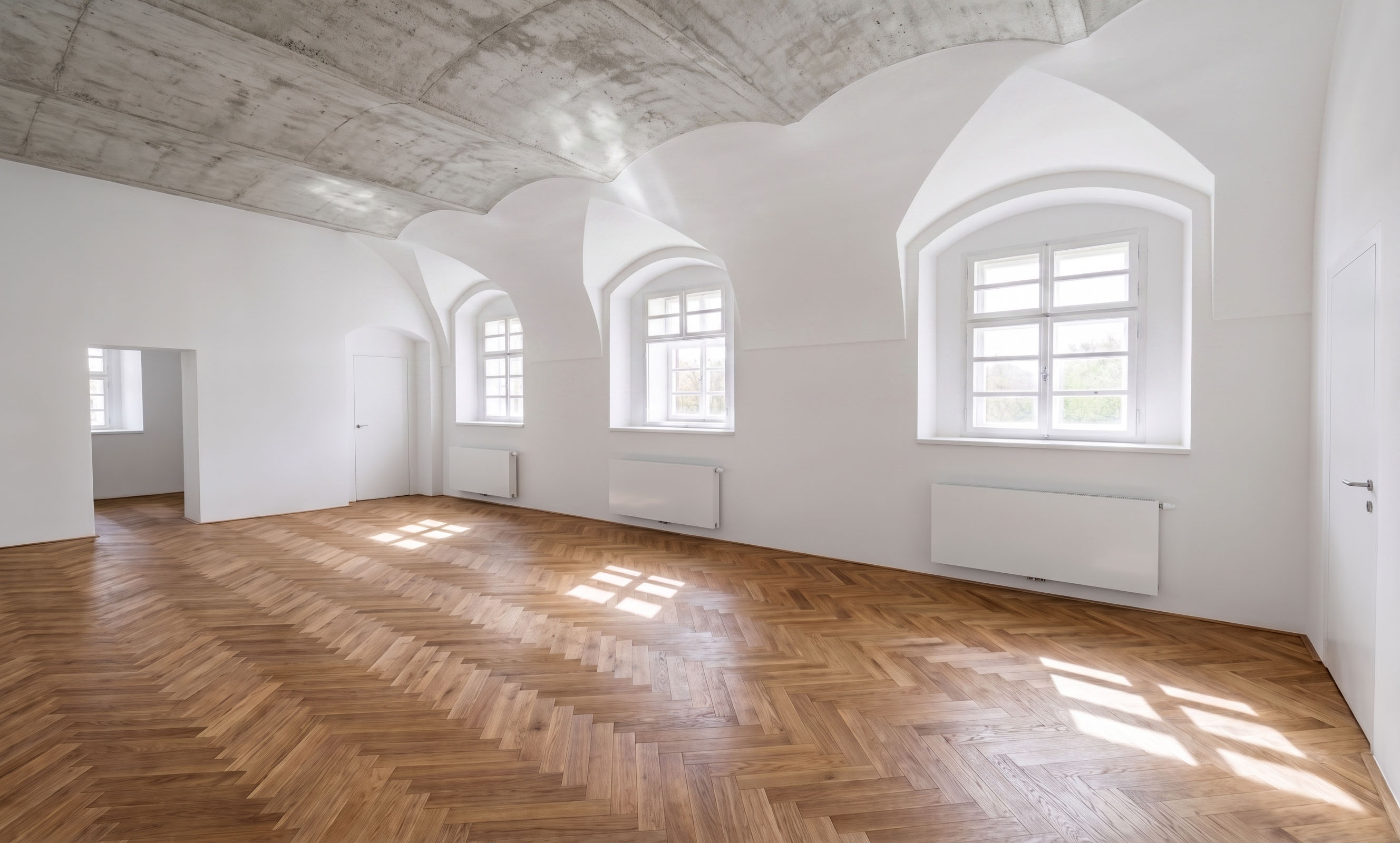 Dlouhý klenutý pokoj se třemi okny a parketovou podlahou